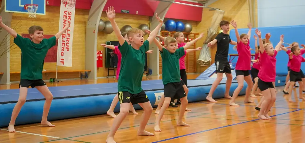 Børn træner gymnastik i Skallerup Hallen med Skallerup-Vennebjerg IF banner i baggrunden